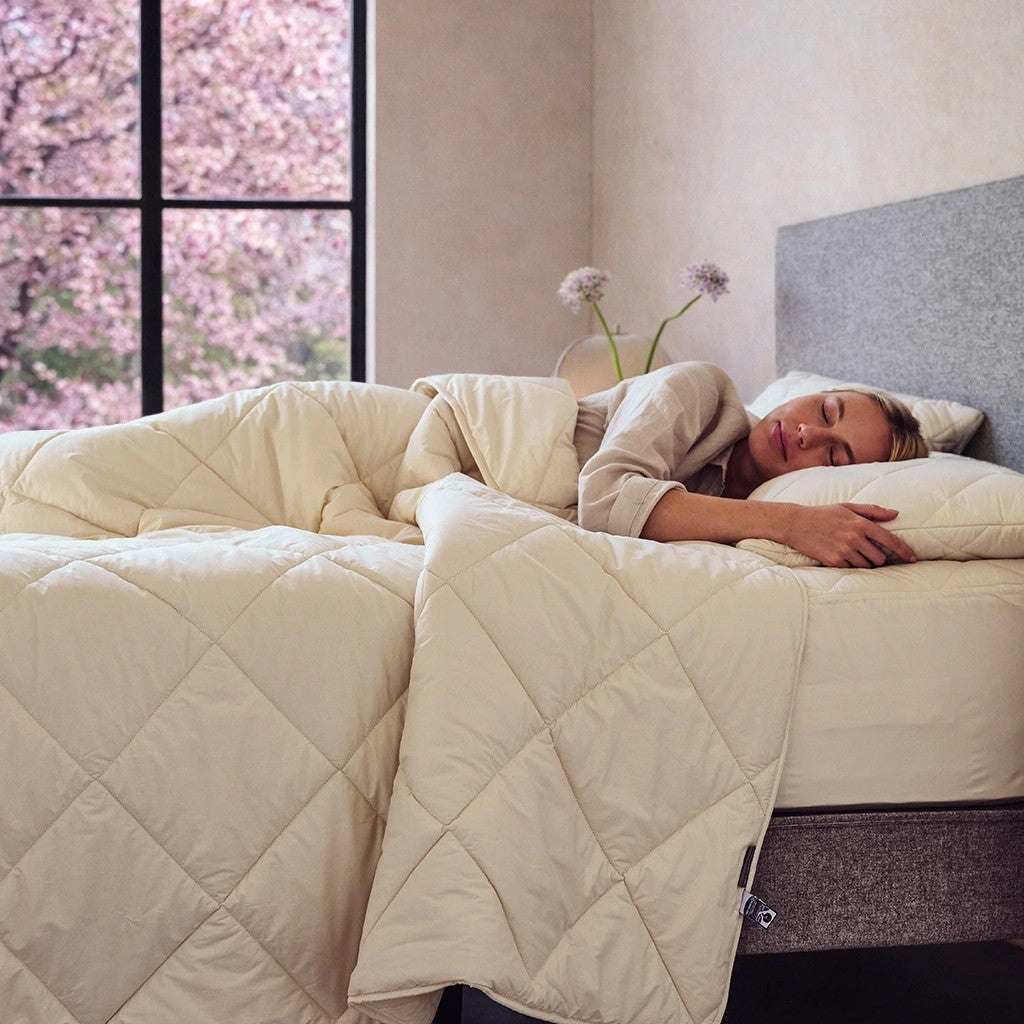 woman sleeping under cream quilted bedding in a bright bedroom