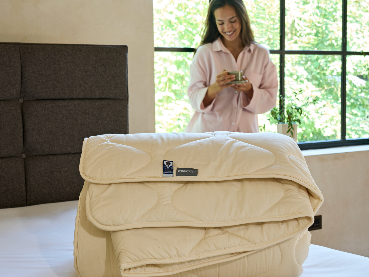 a woolroom comforter rolled up and placed on an empty bed 