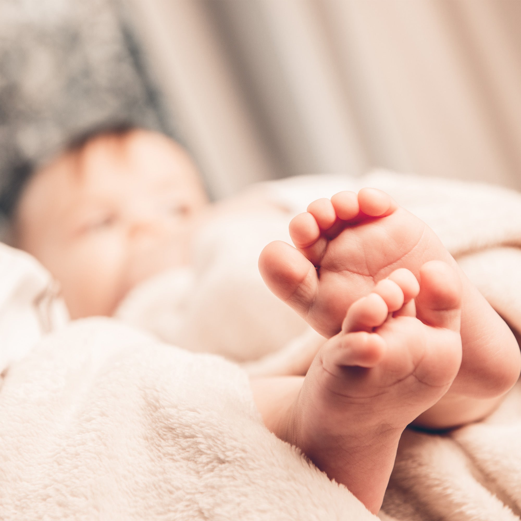 out of focus baby is lying in bed. Focus is on baby's feet.