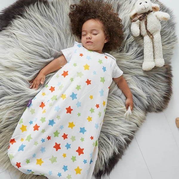 Sleeping baby in polkadot rainbow sleep suit on fluffy bed with toy bunny