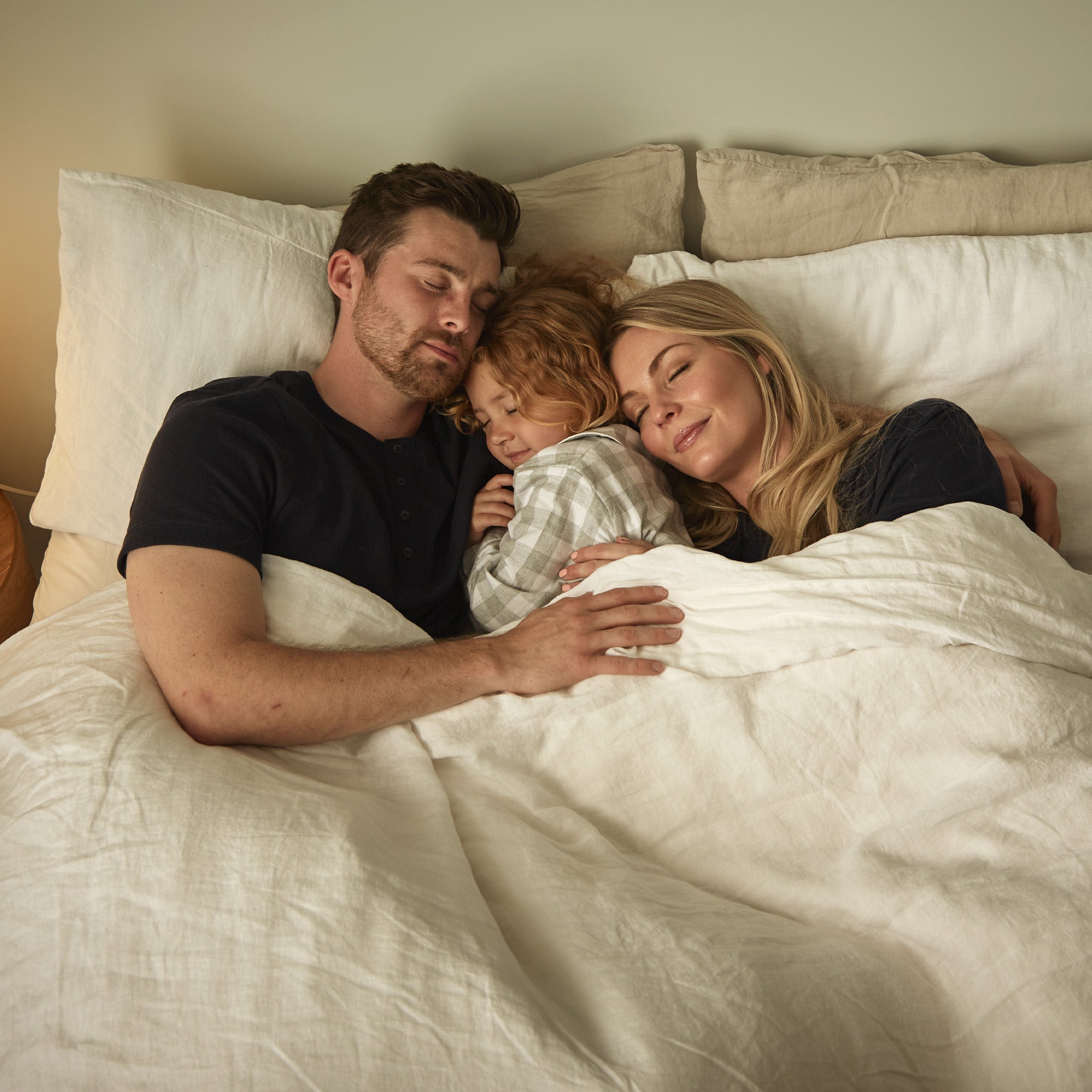 young child is sleeping between mother and father in their bed