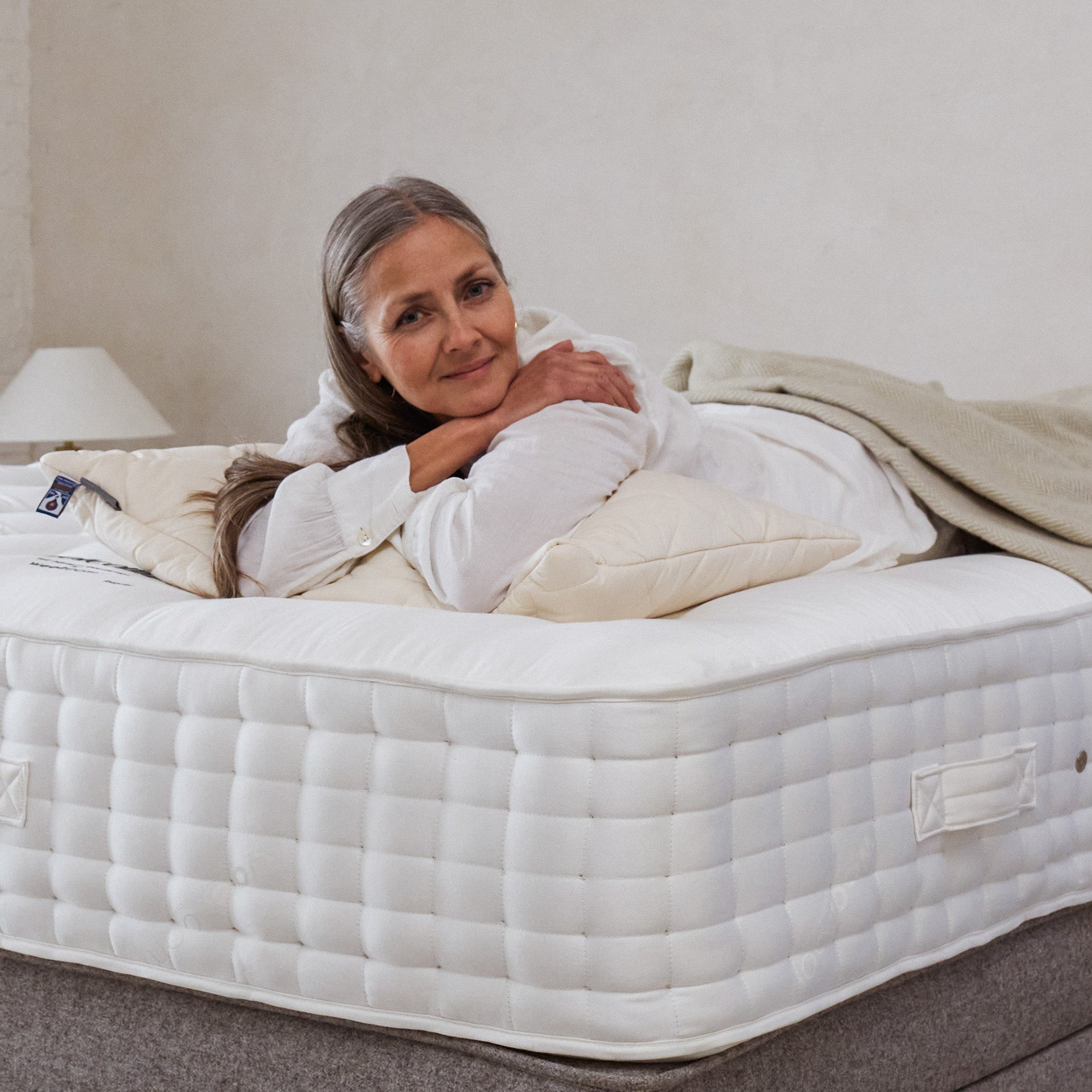 woman lying on her front on a Woolroom Holcombe mattress, she is facing the camera and smiling