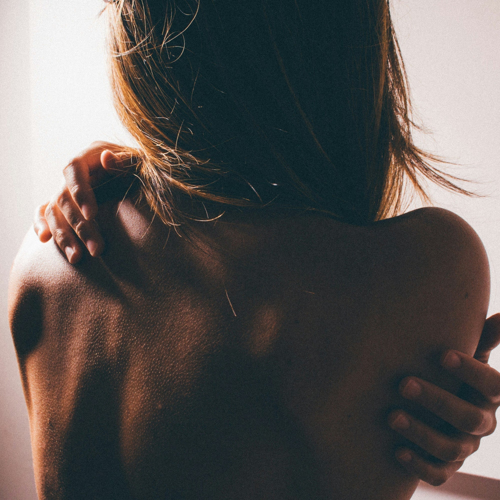 Woman's upper torso from behind. She is scratching her back.