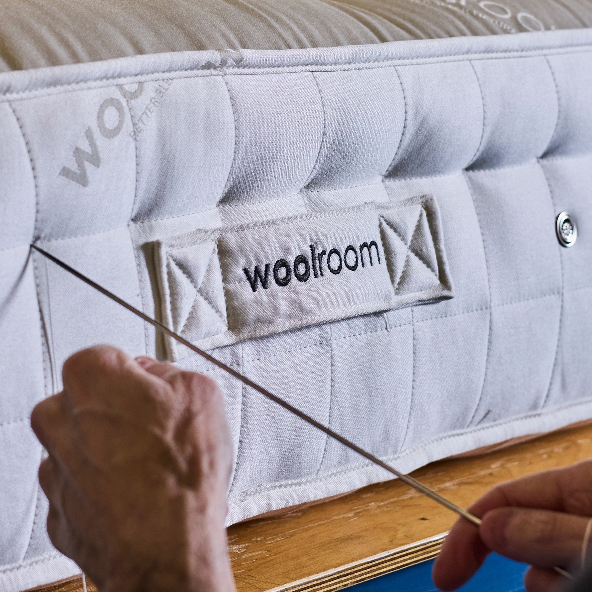 A Woolroom mattress being hand side-stitched. A needle is being pushed into the side.