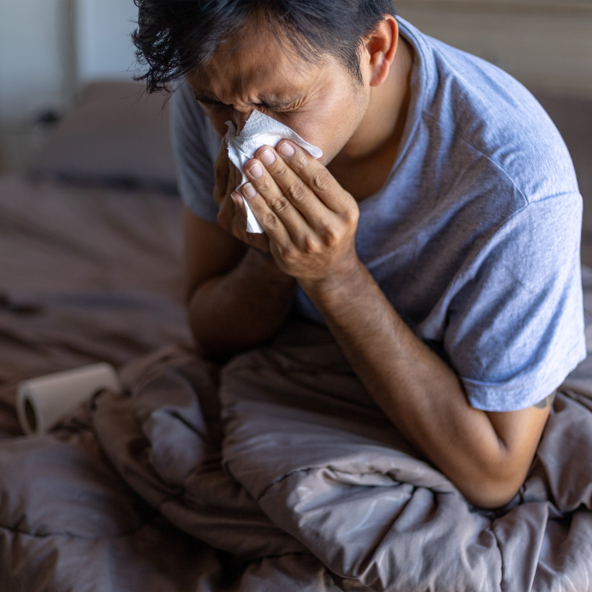 Man sitting in bed blowing nose into tissue 
