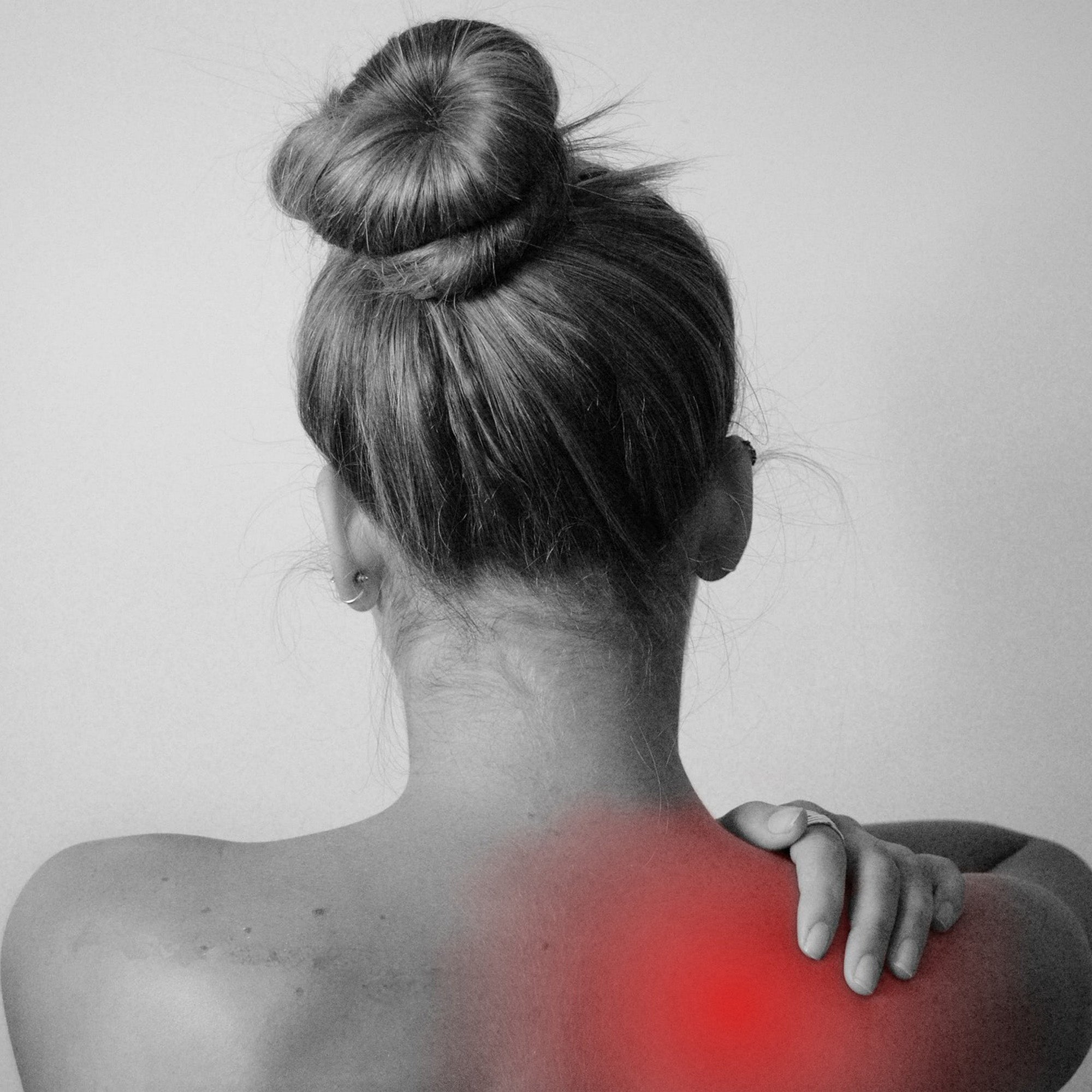 Woman holding her shoulders. There is a red spot indicating pain/inflammation.