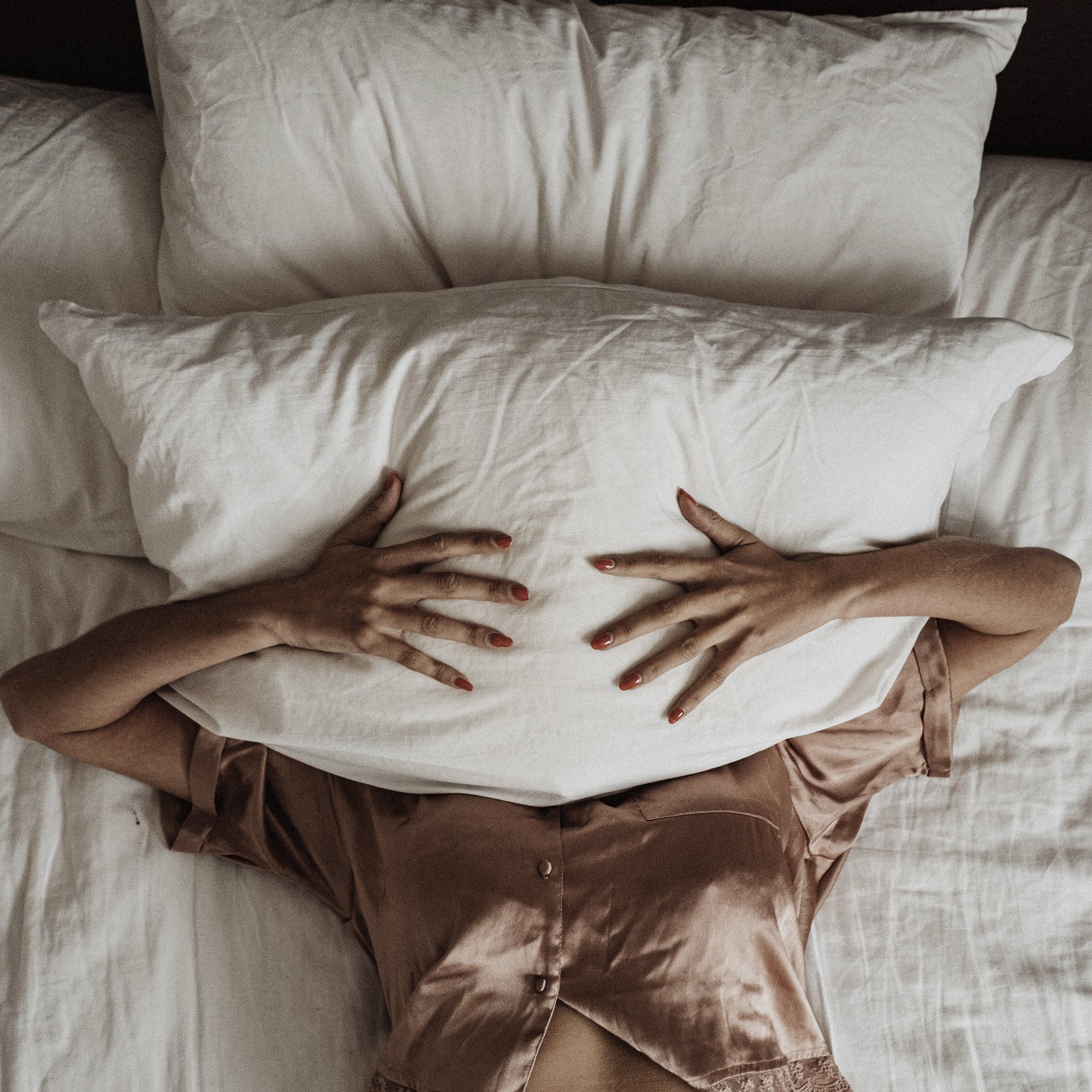 woman in bed  holds a pillow in front of her face