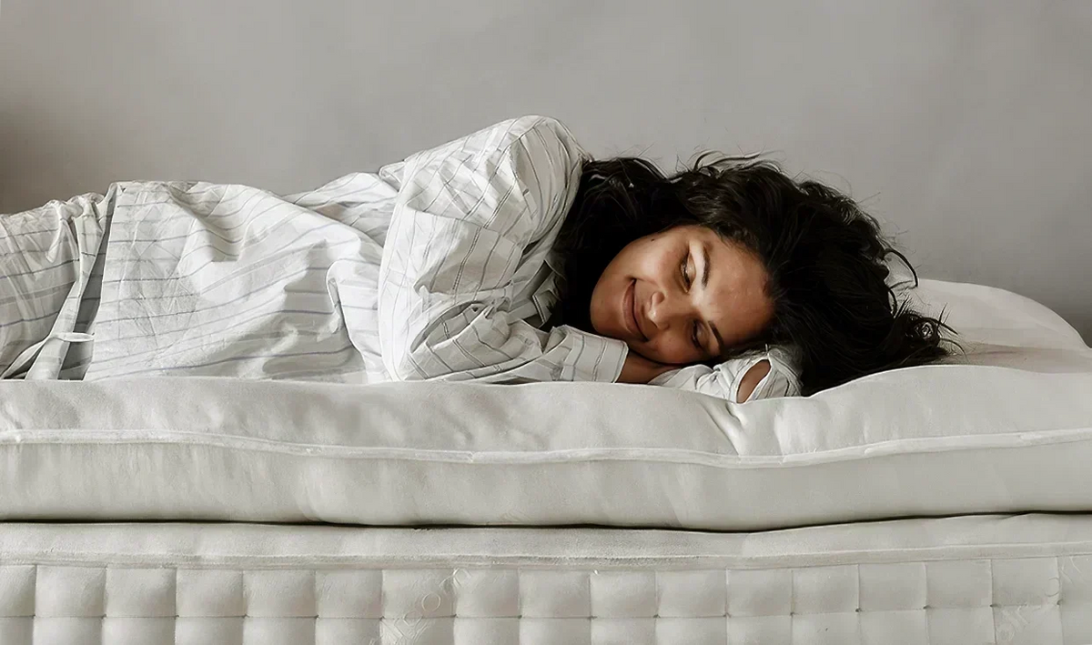 Woman lying on her side smiling with eyes closed, resting on a wool mattress and pillow.