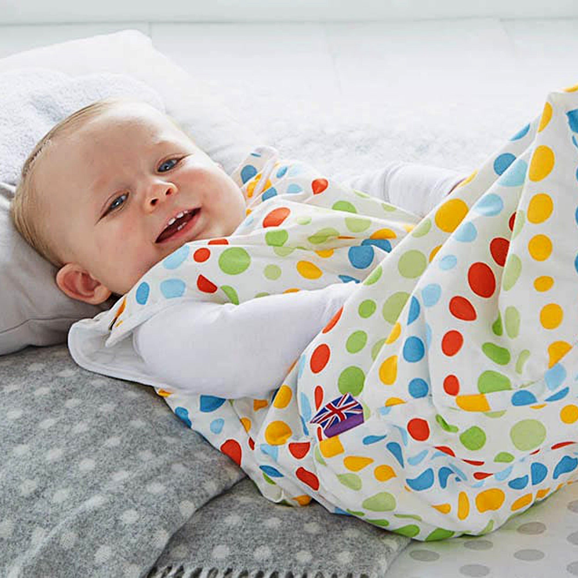 baby in a multicoloured, spotty baby sleeping bag