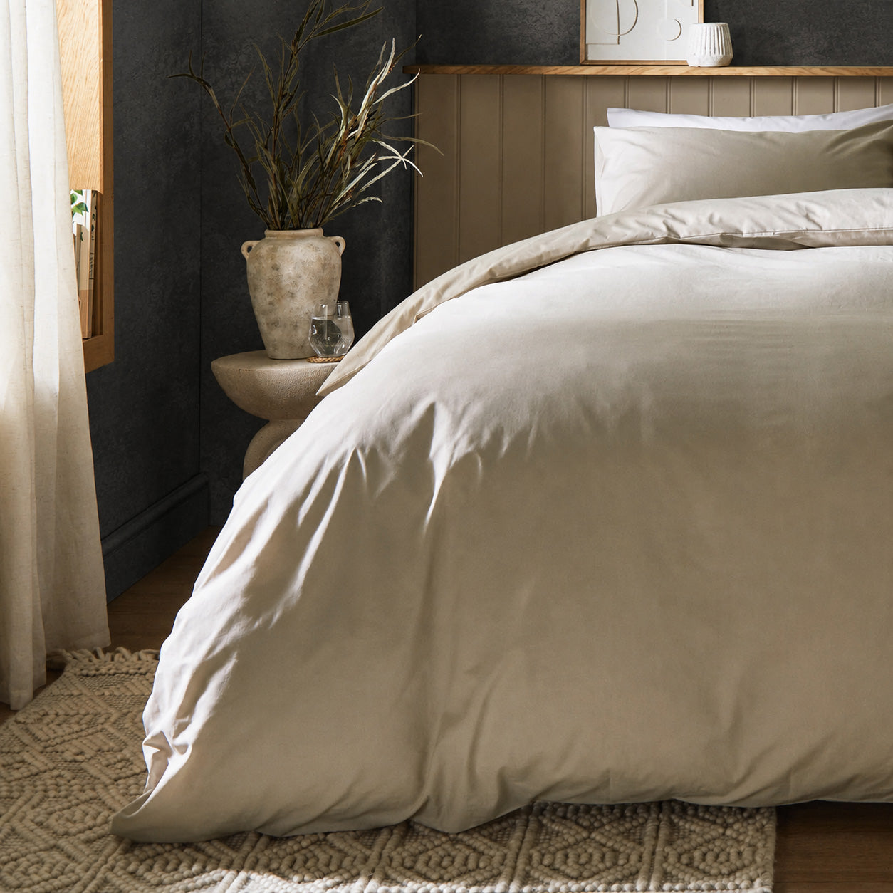 A dressed bed with Woolroom's Arinta's Organic Cotton Duvet Cover in Almond has the duvet turned down and two pillows. 
