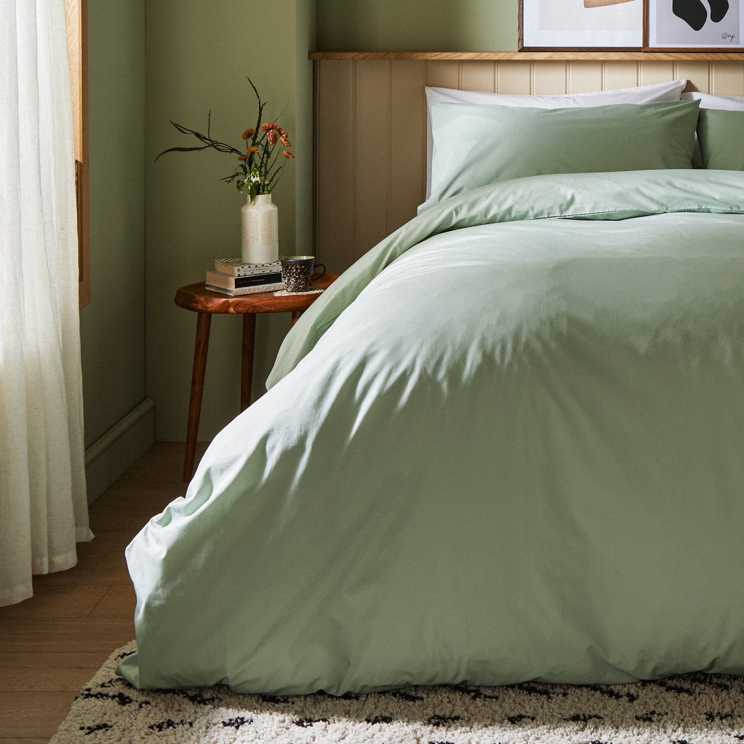 A dressed bed with Woolroom's Arinta's Organic Cotton Duvet Cover in Pistachio has the duvet turned down and two pillows. 