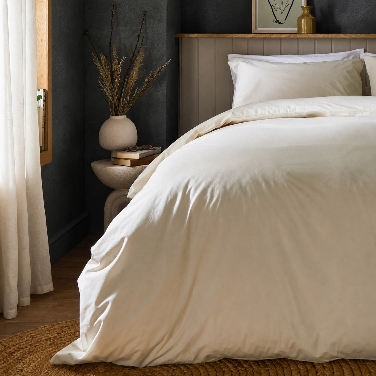 A dressed bed with Woolroom's Arinta's Organic Cotton Duvet Cover in Vanilla has the duvet turned down and two pillows. 