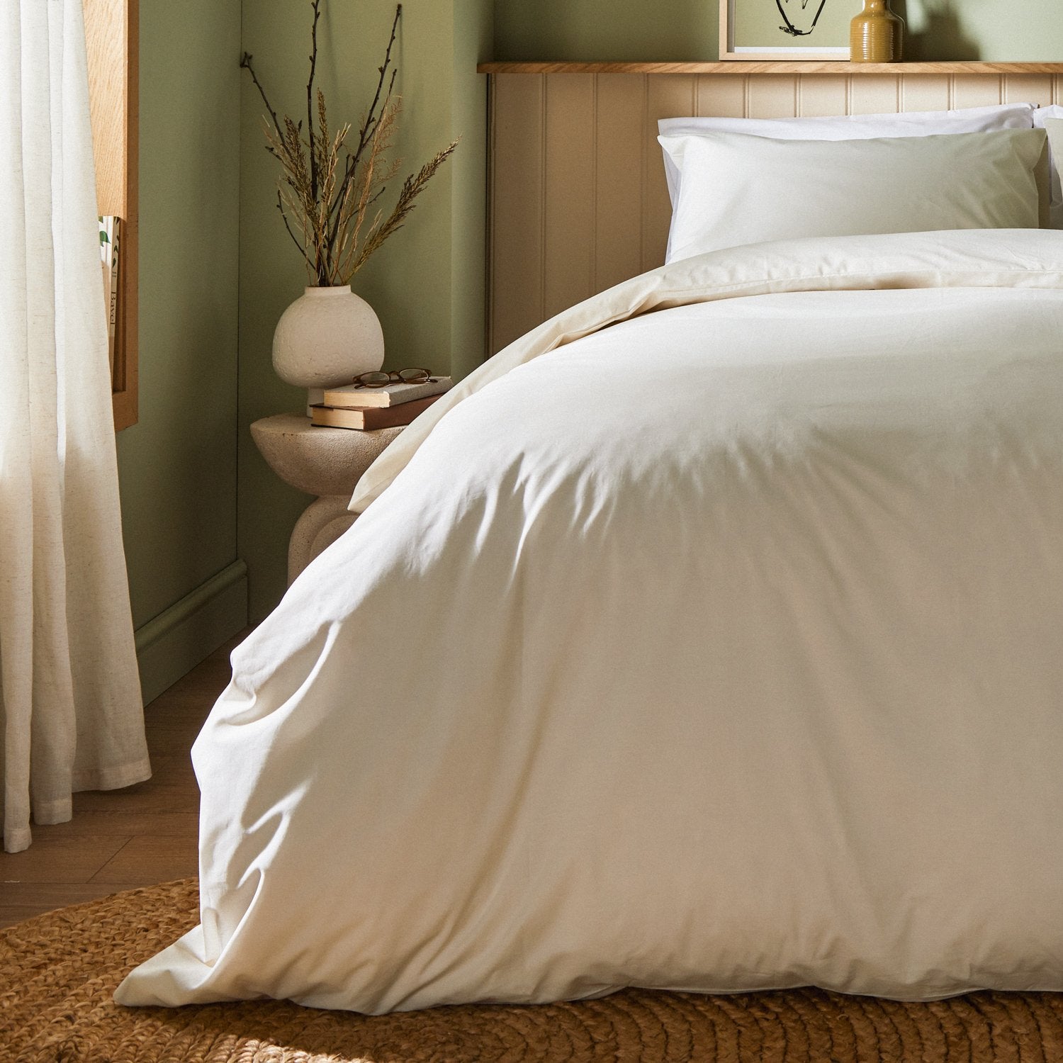 A dressed bed with Woolroom's Arinta's Organic Cotton Duvet Cover in Vanilla has the duvet turned down and two pillows. 