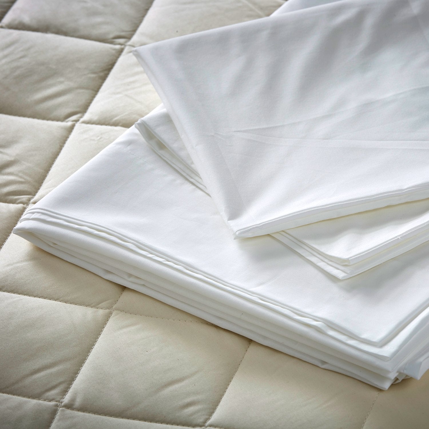 The Arinta Organic Cotton flat sheet in white folded and pressed on a bare mattress. 