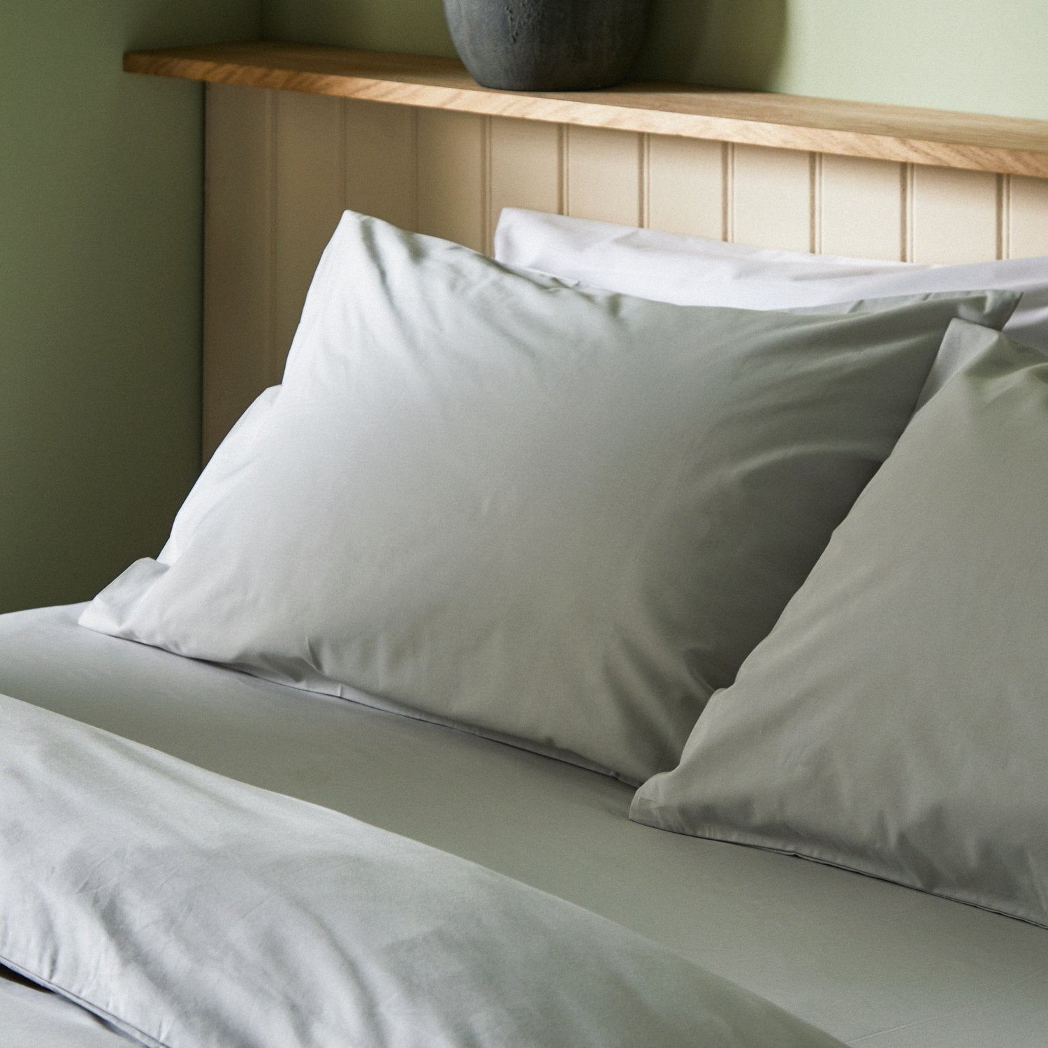 Four pillows on a dressed bed with Arinta Organic Cotton Pillow Cases in Earl Grey.