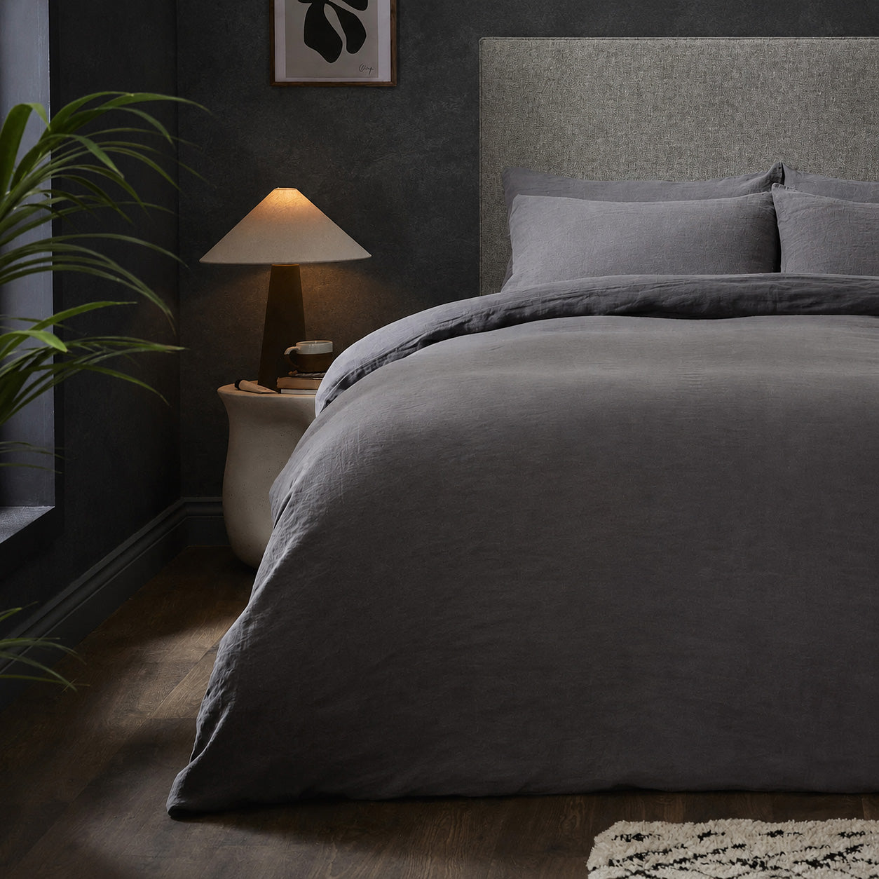 A dressed bed with Woolroom's Mariana Linen Duvet Cover in Charcoal has the duvet turned down and two pillows. 