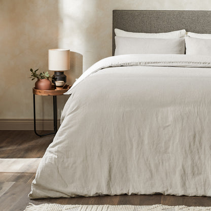 A dressed bed with Woolroom's Mariana Linen Duvet Cover in Pebble has the duvet turned down and two pillows. 
