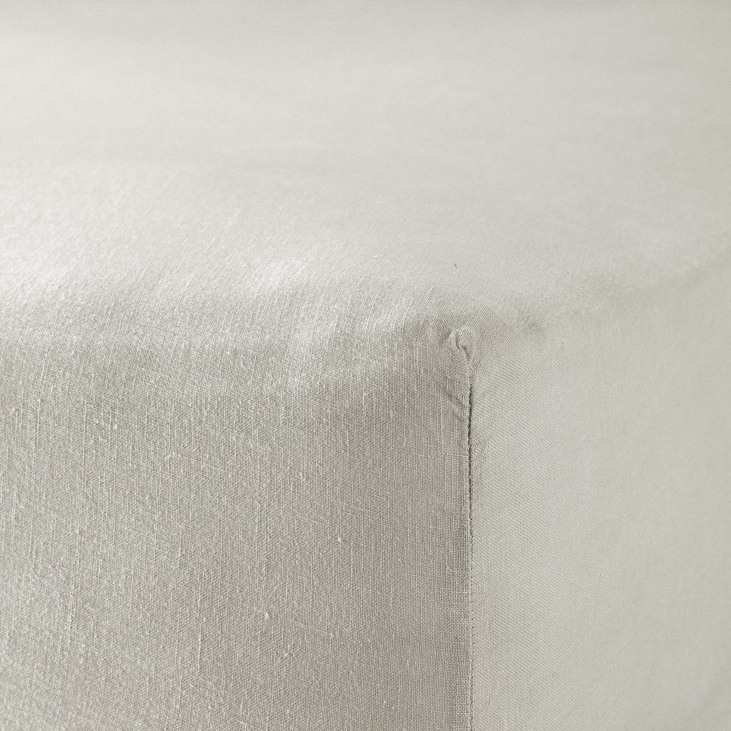 A close up of the corner of a mattress with Woolroom's Mariana Linen Blend Fitted Sheet in Pebble.