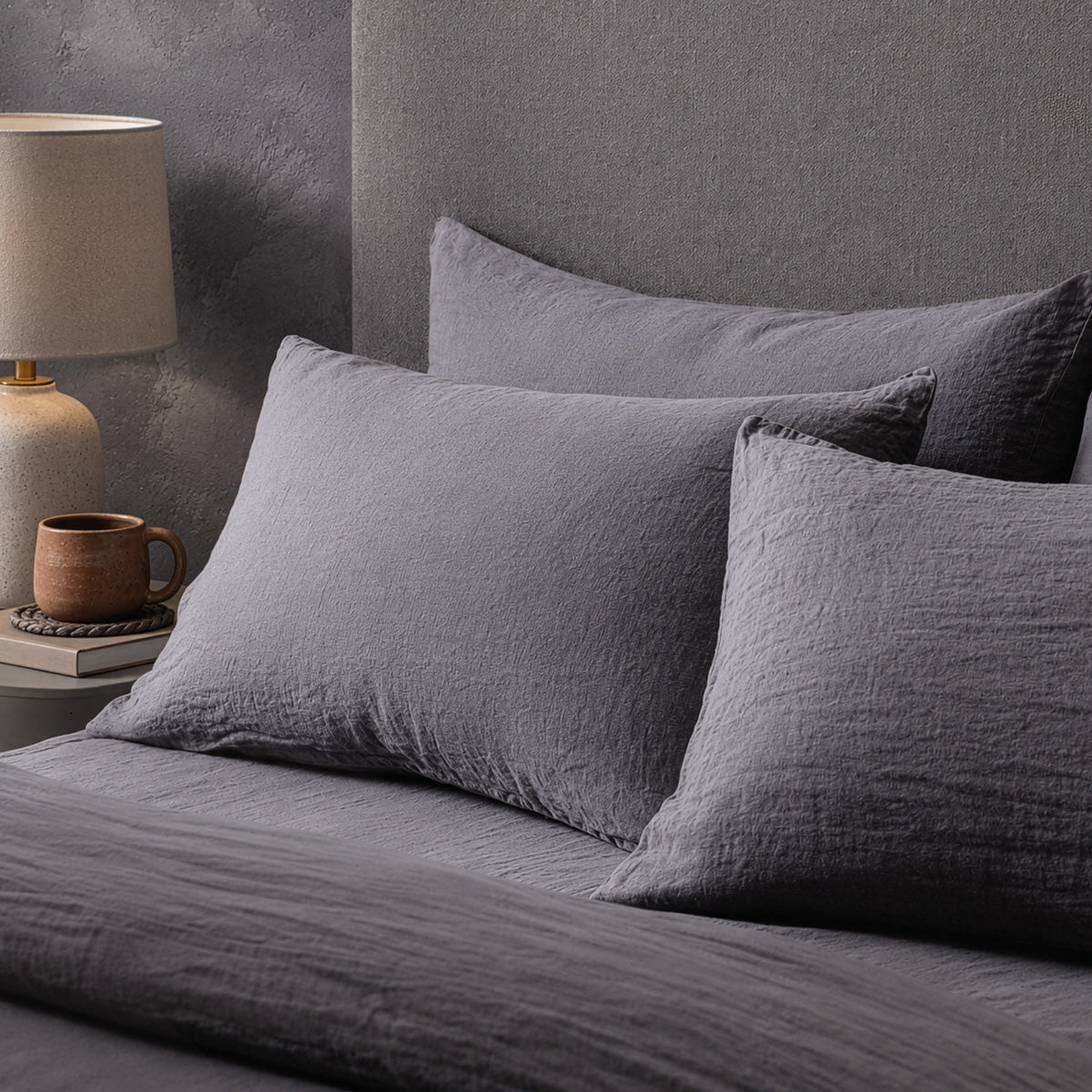 Four pillows on a dressed bed with the Mariana Linen Blend Pillow Cases in Charcoal.