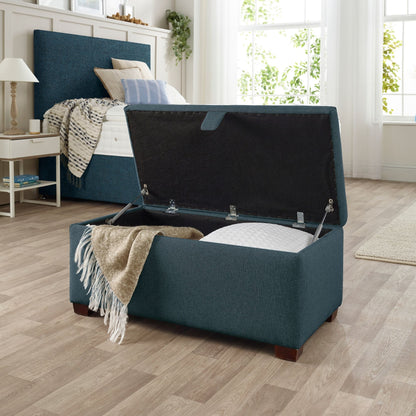 The Woolroom Ottoman Storage Box in Hemlock blue upholstery stores pillows and throws and other items. 