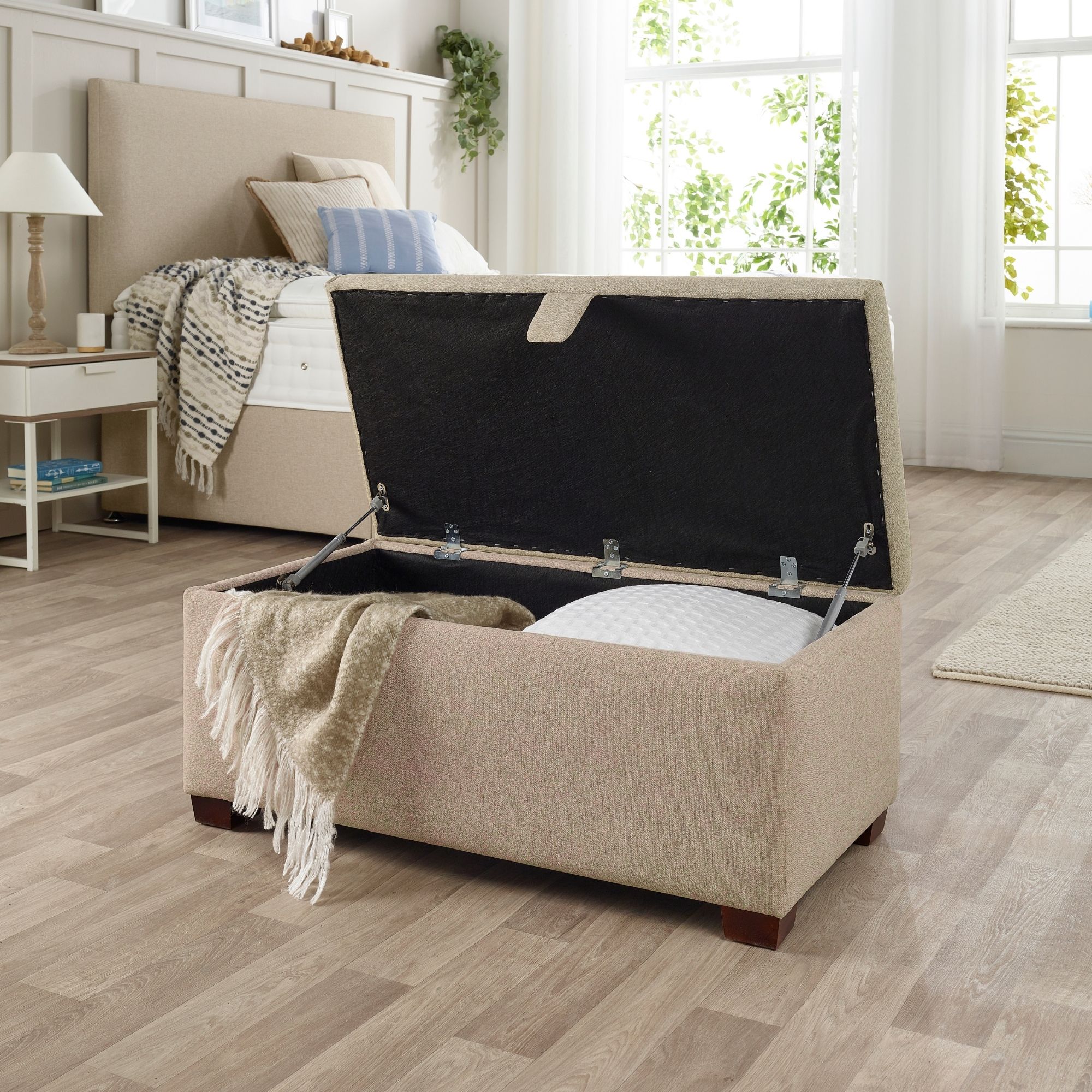 The Woolroom Ottoman Storage Box in Walnut brown upholstery stores pillows and throws and other items. 