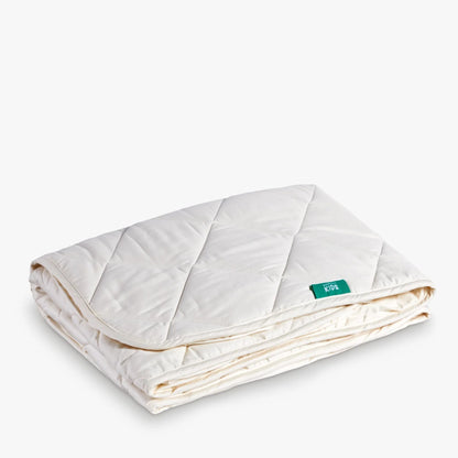 A folded Woolroom Organic Washable Wool Kids Mattress Protector, which fits on top of a bare mattress for coverage.
