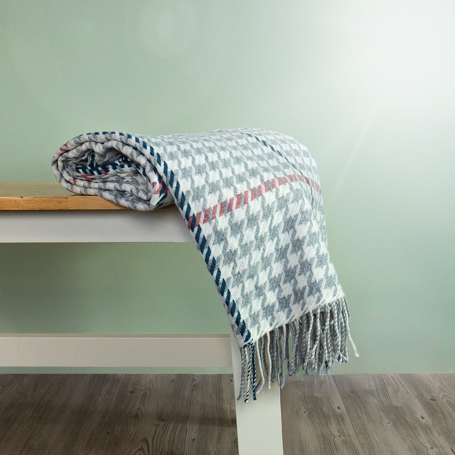 The Carroglen Wool Throw in colour Silver is a grey and white houndstooth pattern, shown folded on a bench. 