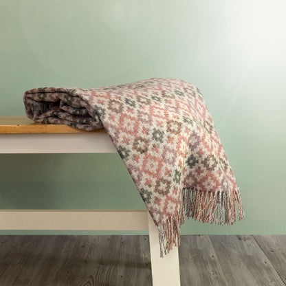 The Dartmouth Wool Throw in Coral is a unique cross and square pattern and fringe, shown folded on a bench. 