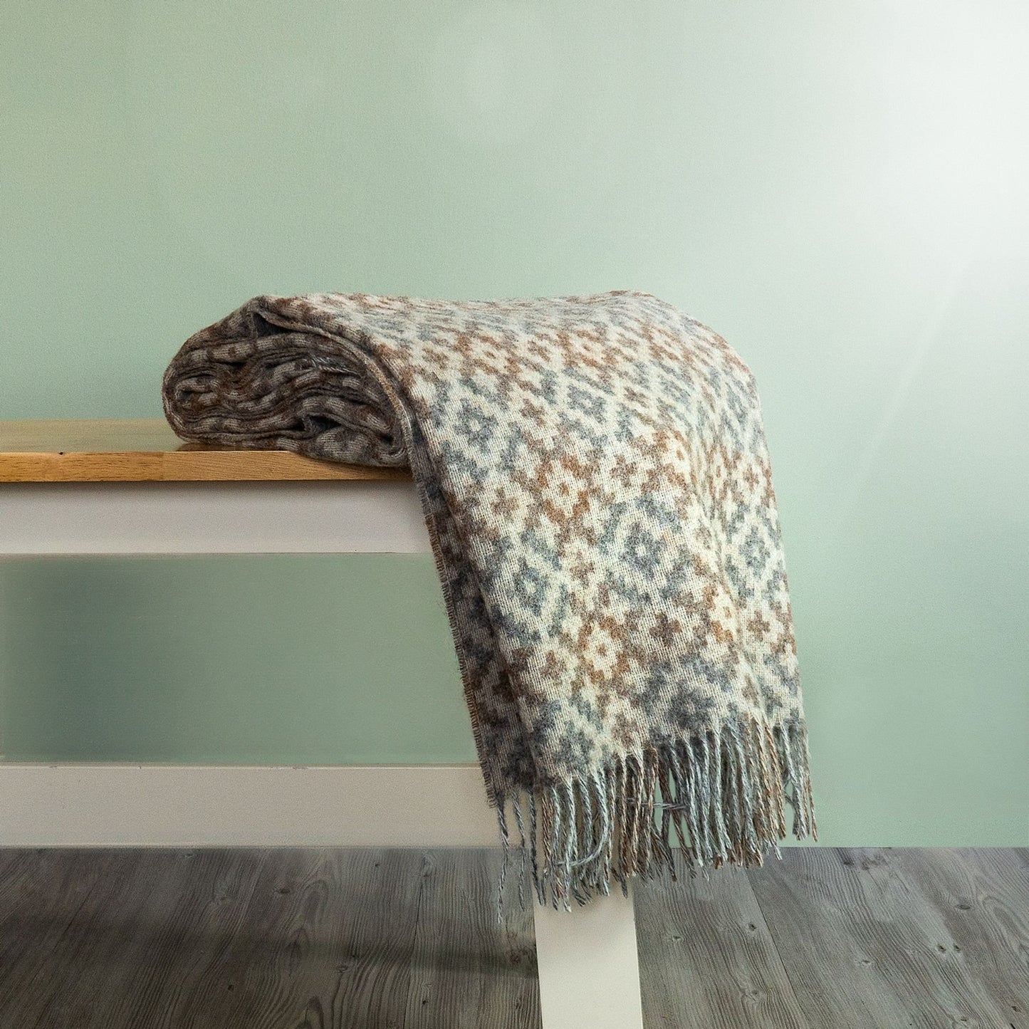 The Dartmouth Wool Throw in Natural is a unique cross and square pattern and fringe, shown folded on a bench. 