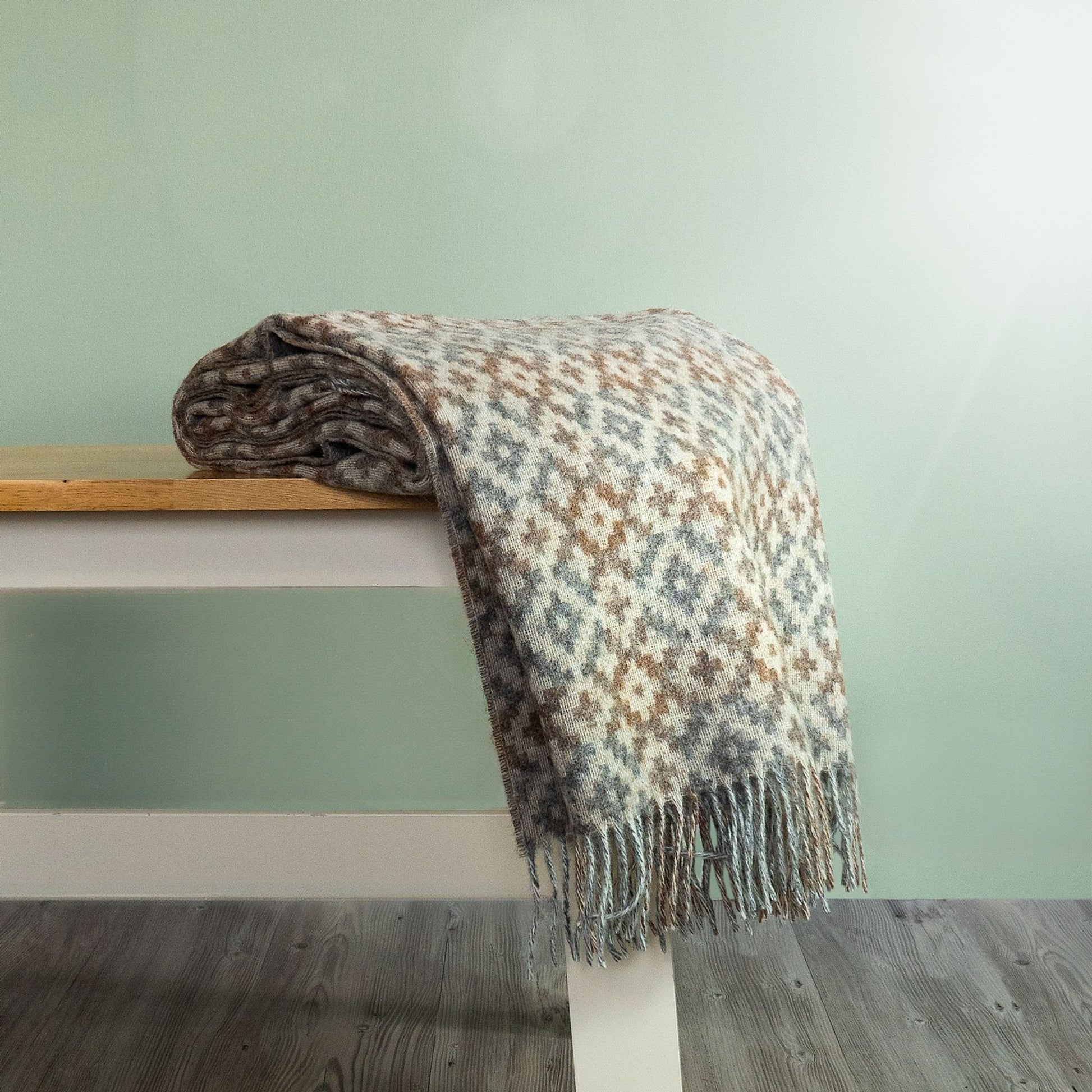 The Dartmouth Wool Throw in Natural is a unique cross and square pattern and fringe, shown folded on a bench. 
