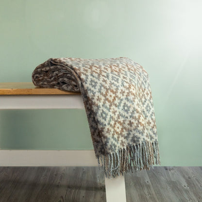 The Dartmouth Wool Throw in Natural is a unique cross and square pattern and fringe, shown folded on a bench. 
