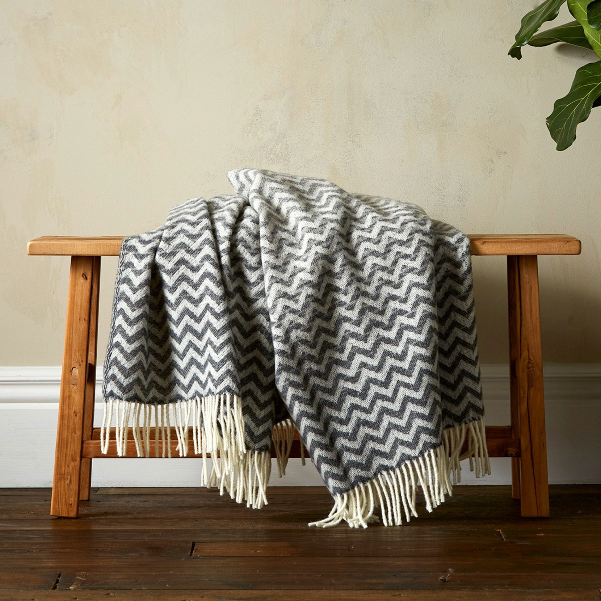 The Woolroom Astrid Gradient Pure New Wool Throw in colour Grey, draped on a bench with fringe. 