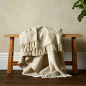 The super soft Greta Herringbone Wool Blanket in Beige draped over a bench with the white fringe.