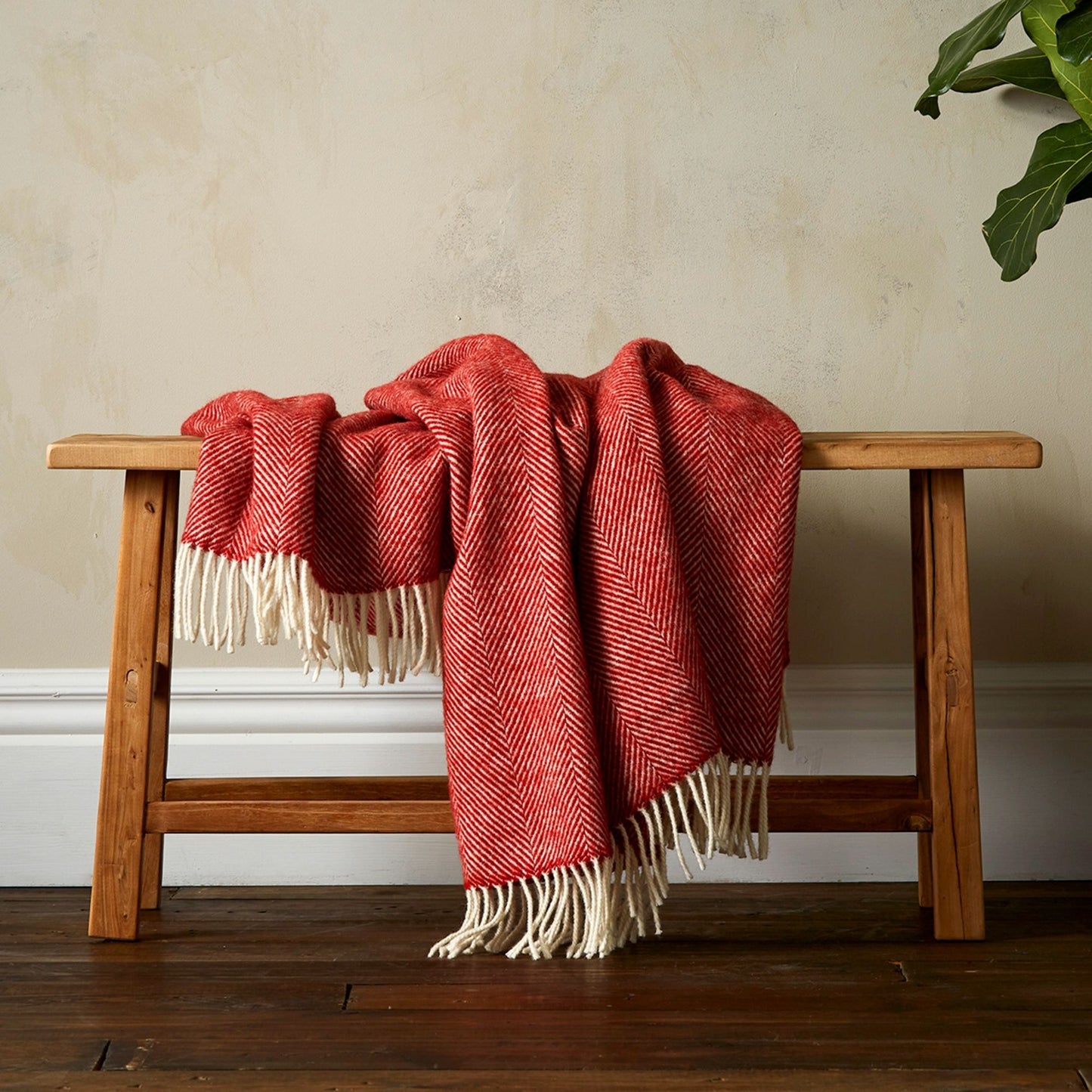 The super soft Greta Herringbone Wool Blanket in Terracotta draped over a bench with white fringe. 