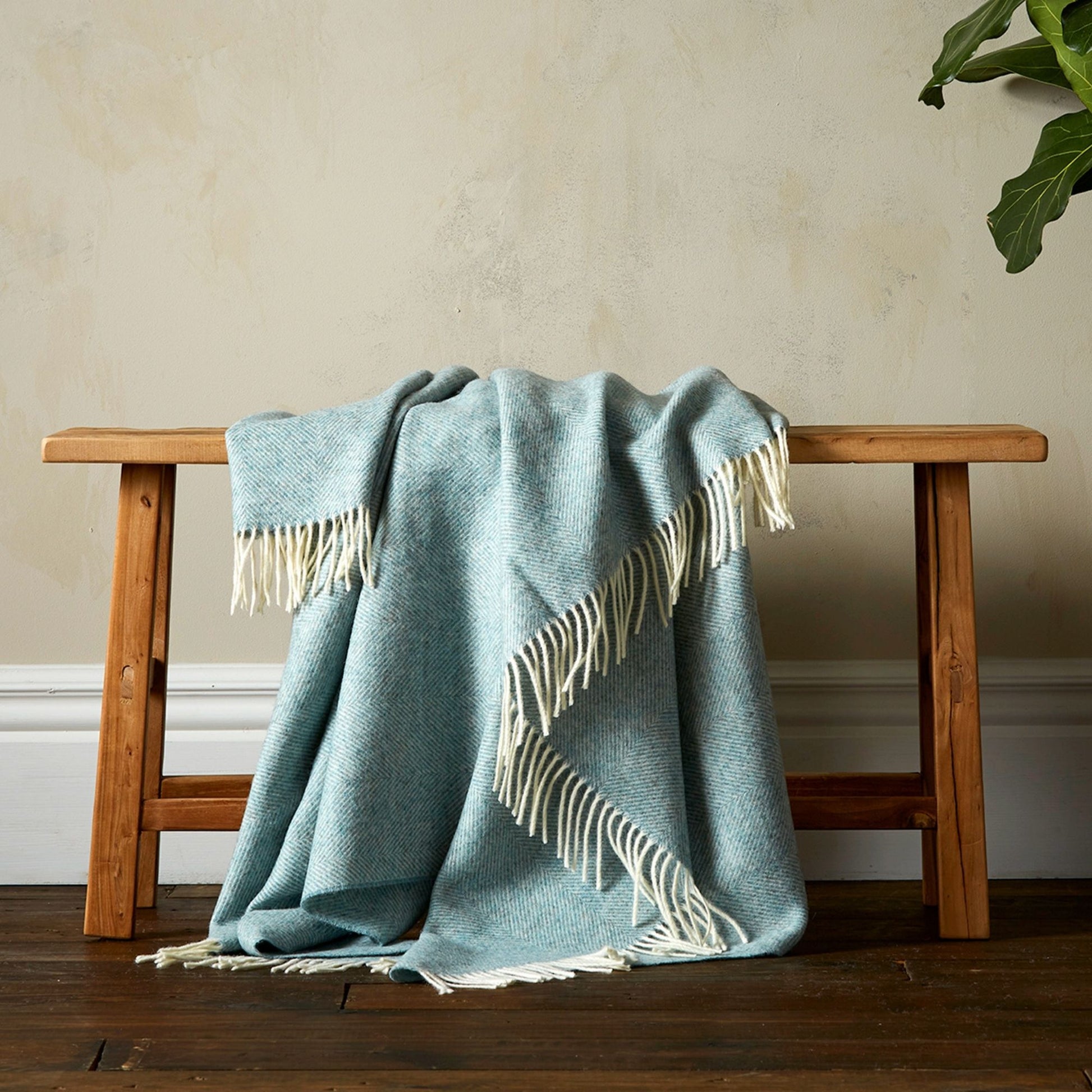 The Herringbone Shetland Throw in color Duck Egg with white fringe, draped over a bench. 