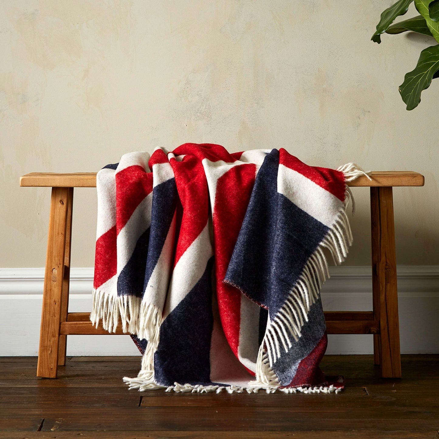 The Woolroom Union Jack Merino Throw in Red, White & Blue is a quintessential British blanket, shown draped on a bench.