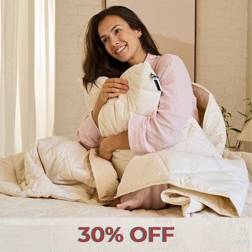 A brunette lady stretching in bed, laying under a Woolroom duvet