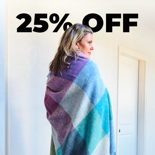 A collection of blue, green, red, beige and yellow wool throws draped over a wooden banister in a home.