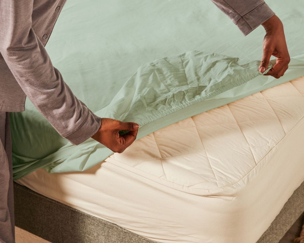 Person adjusting a fitted sheet on a bed