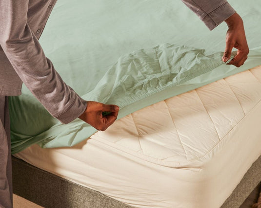 Person adjusting a fitted sheet on a bed