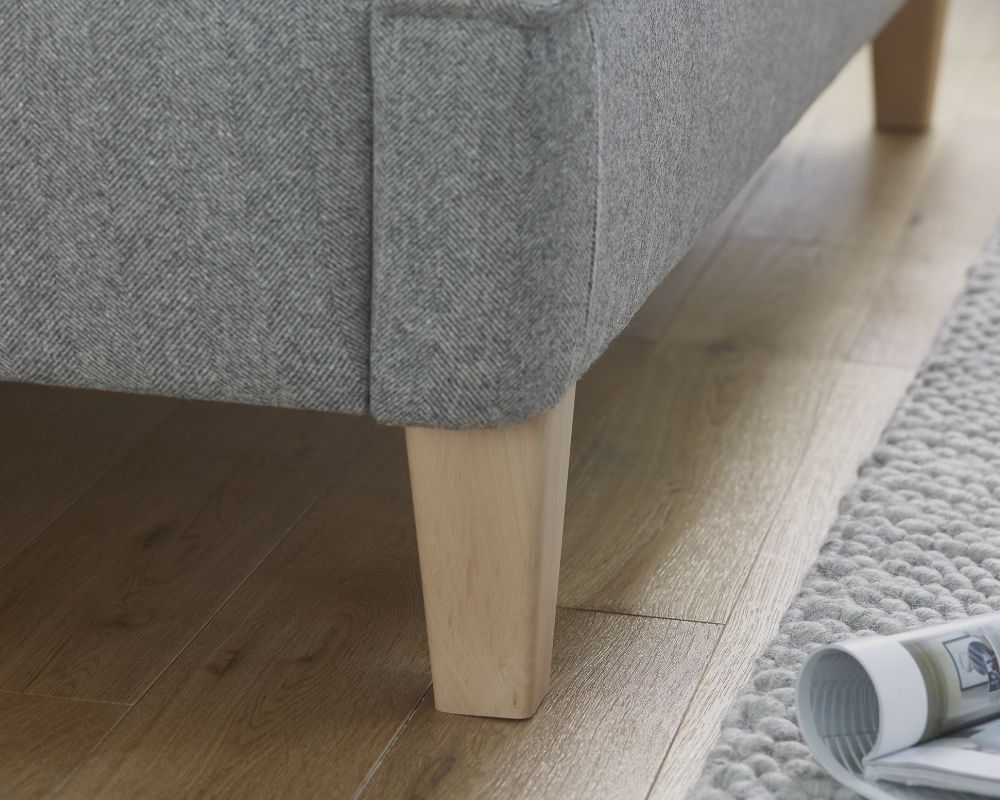 Gray upholstered bed with wooden legs on a wooden floor.