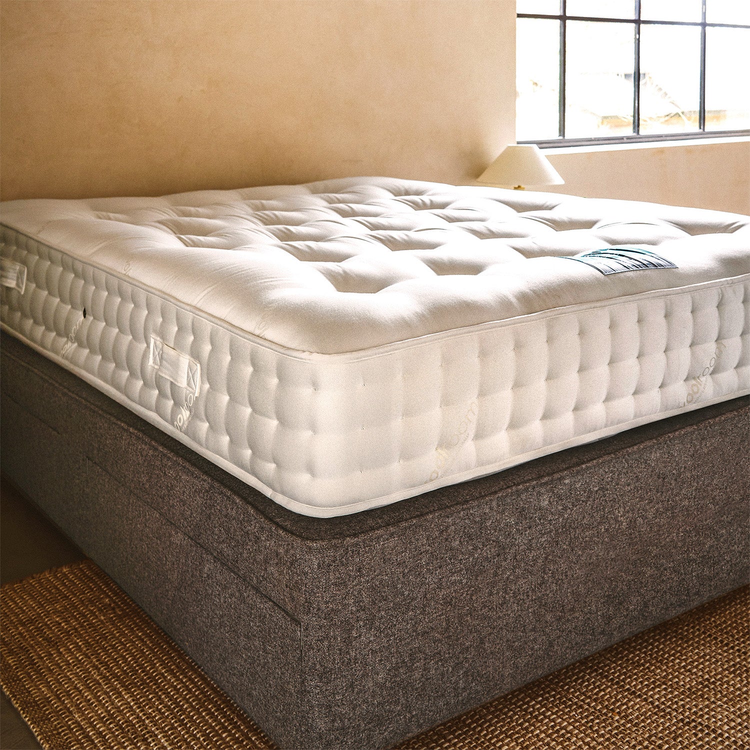 A white quilted wool mattress with a Woolroom label, shown on an upholstered divan base.