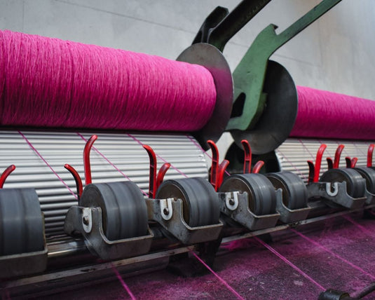 Textile machine with pink yarn on rollers in a factory setting