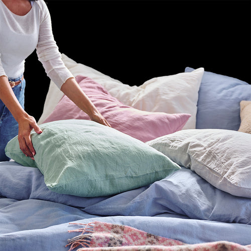 woman arranging pillows covered in multiple linen colours