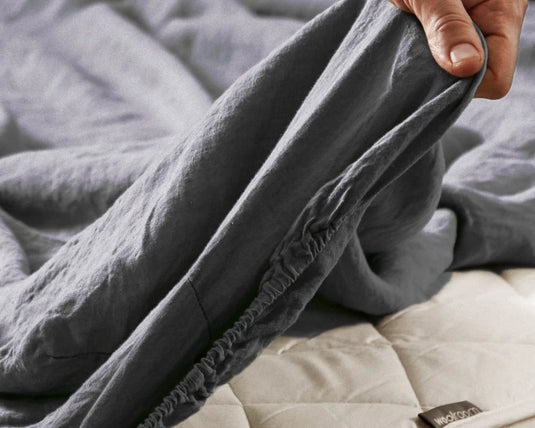 Gray weighted blanket being held over a mattress with a brand label visible.