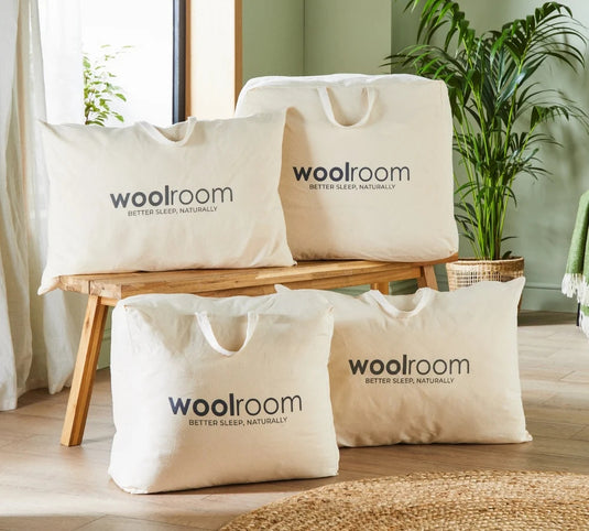 Woolroom bags displayed on a wooden bench with a plant and chair in the background.