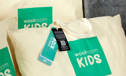 Woolroom Kids products including a pillow, tote bag, and tags on a neutral background