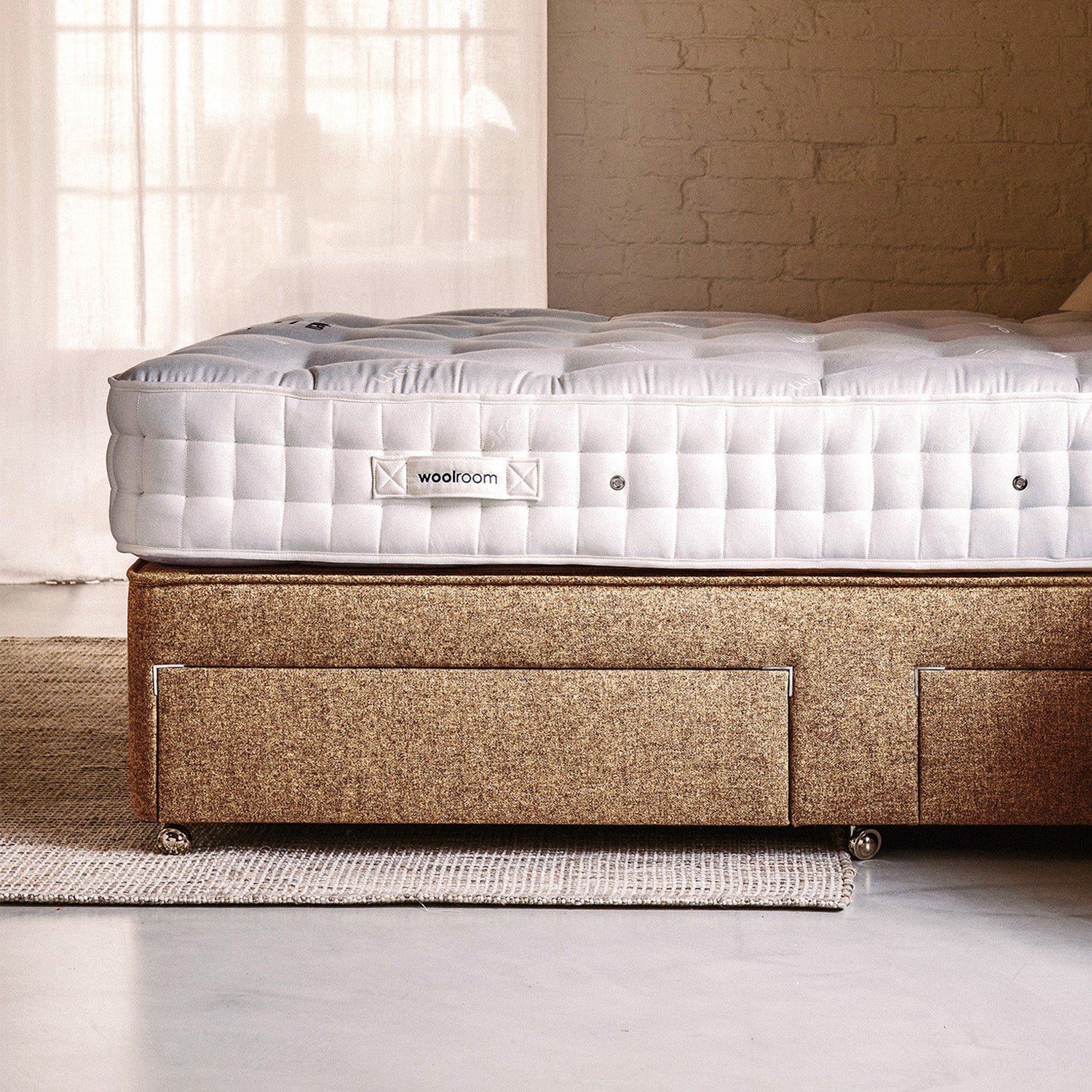 A white quilted wool mattress with a Woolroom label, on a tan tweed divan base with drawers.