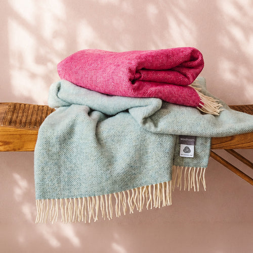 A collection of blue, green, red, beige and yellow wool throws draped over a wooden banister in a home.