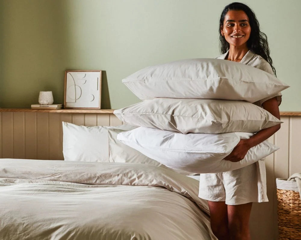Woman holding a stack of pillows in a bedroom setting